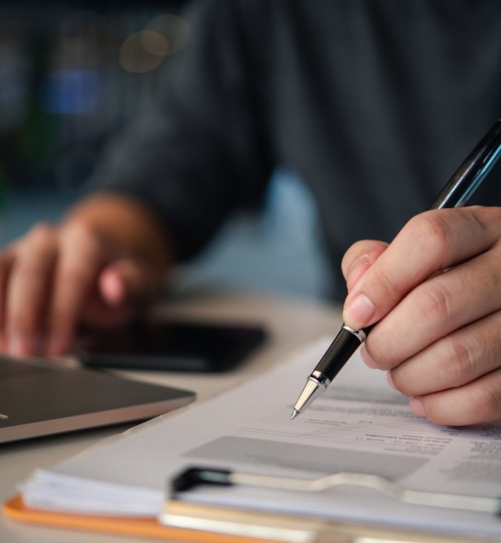 Closeup of a man's hand holding a pen, writing on papers.